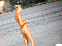 Seducing beach nudist blonde is staying in the middle of the resting crowd shdowing even the sun with the body beauty